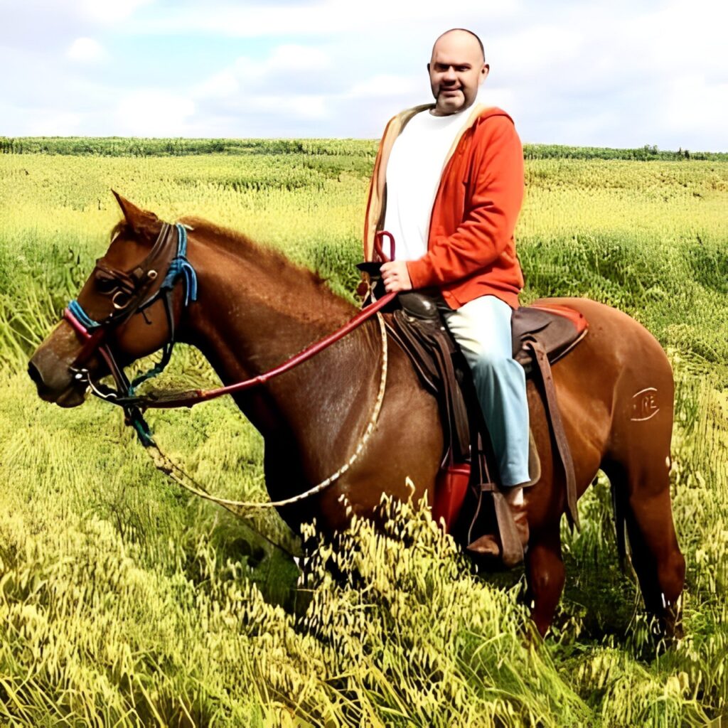 Eu andando a cvalo na fazenda da minha cunhda no Paraná. É uma foto recente estou de calça jeans, camiseta branca, moleton aveludade alaranjado escuro... Sob a relva. Com o céu crispado de nuvens. É um dia claro.